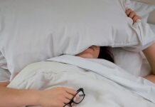 수면의 질이 건강을 좌우한다…숙면을 위한 생활습관의 중요성 person lying on bed while covering face with pillow and holding eyeglasses