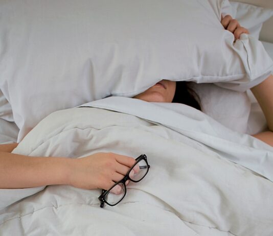 수면의 질이 건강을 좌우한다…숙면을 위한 생활습관의 중요성 person lying on bed while covering face with pillow and holding eyeglasses